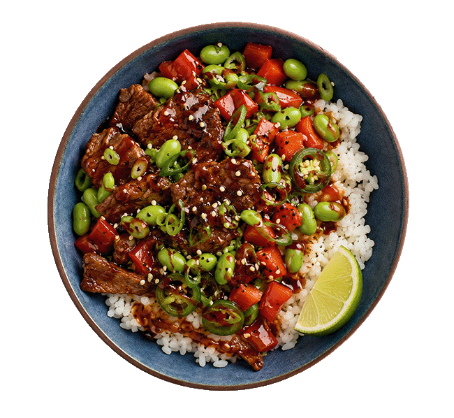 Eine runde, dunkle Schale von oben fotografiert, gefüllt mit weissem Sushi-Reis, gebratenem Rindfleisch in dunkler Sauce, roten Paprikastücken, grünen Edamame, Sesam und einer frischen Limettenspalte.